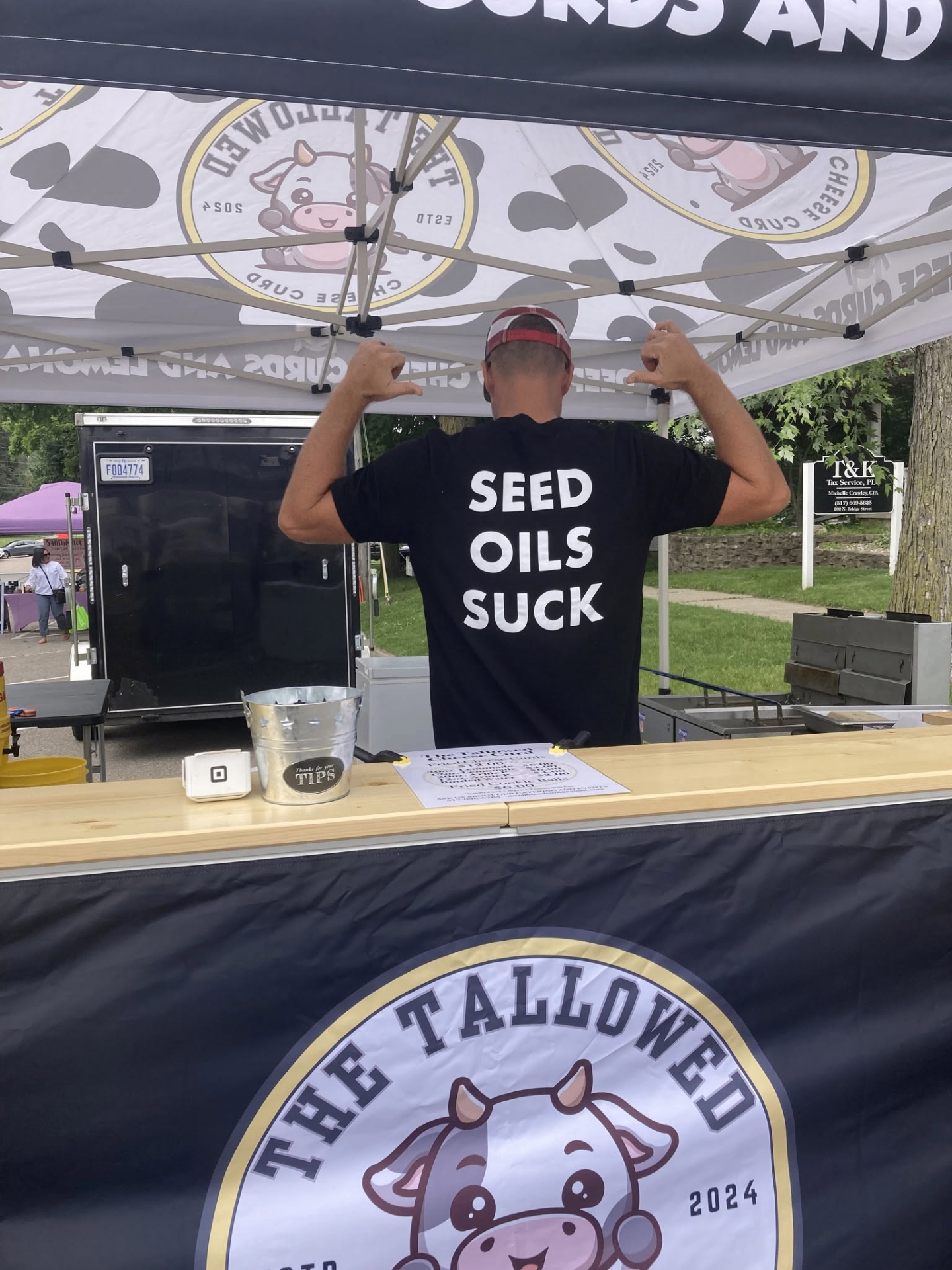 Crew member at the booth wearing a 'Seed Oils Suck' shirt — fried in pure beef tallow